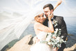 Wedding couple, groom, bride with bouquet posing near sea and blue sky
