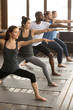 © fizkes - Group of young sporty afro american and caucasian people practicing yoga lesson, standing in Warrior two exercise, Virabhadrasana II pose, working out, indoor, studio