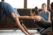 © fizkes - Smiling yoga teacher or pilates instructor helping young man to stretch muscles holding hands on his shoulders, sporty fit guy doing downward facing dog exercise with trainer at group class training
