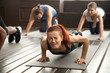 © fizkes - Young fit sporty woman with painful face expression doing hard difficult plank fitness exercise or push press ups feeling pain in muscles at diverse group training class in gym, endurance concept