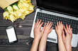 Business woman and little son using laptop computer in office. Woman and baby hands typing on laptop keyboard near mobile smart phone and bouquet of tulips. Top view, flat lay