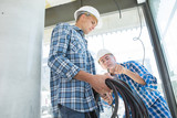 Fototapeta  - two builders in helmets working with electricity indoors