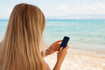 Smartphone woman texting on social media app looking at display screen for sms reading on ocean background on a sea cruise balcony or beach at sunset on holiday. Unrecognizable girl using smart phone.