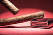 Two Cuban cigars and a lighter on a red background with a light from above