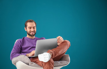 Sticker - Handsome man with laptop sitting in comfortable armchair against color wall