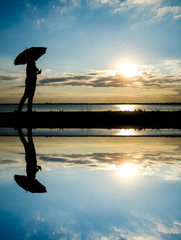 Wall Mural - silhouette woman hold umbrella walking on road with water reflection