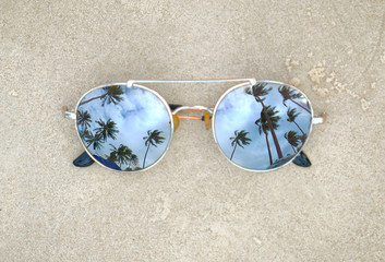 Mirrored sunglasses close up on the beach sand with palm trees reflection