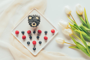 Wall Mural - top view of sweet tasty muffin in shape of bear, fresh raspberries and tulip flowers