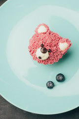 Wall Mural - top view of sweet pink muffin in shape of bear and fresh blueberries on blue plate