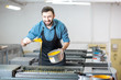 Portrait of a handsome typographer standing with yellow paint for offset machine at the printing manufacturing