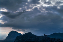 Dark Clouds In The Evening Over The Mountains. Silhouettes Of The Birds In The Sky And Fortress.