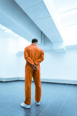 Wall Mural - rear view of prisoner in orange uniform standing in prison cell