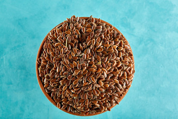 Close-up picture of flax seeds in a clay bowl isolated on blue background.