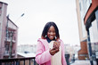 © AS Photo Family - African american girl in red hat and pink coat at street of city against building on winter day with mobile phone.