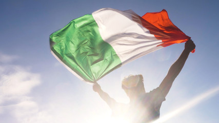 young man holding italian national flag to the sky with two hands at the beach at sunset italy