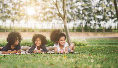 Wall Mural - Happy three little friends laying on the grass in the park. american african children playing Bricks in park