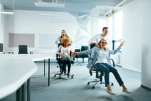 Office. People Having Fun And Racing On Chairs.