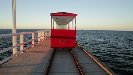 Wall Mural - POV view from behind of vintage red train illuminated by sunset light, going on Jetty Busselton tracks in Busselton town, WA. Busselton Jetty is the longest wooden pier in the world and iconic place.