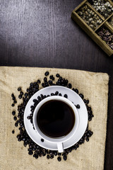 Black coffee in white cup and coffee bean and box on cloth and wood background.