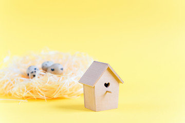 Quail eggs in a straw nest, wooden bird feeder on a yellow background. Easter concept.