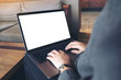 © Farknot Architect - Mockup image of businessman using and typing on laptop with blank white desktop screen on wooden table in cafe
