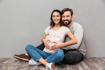 Wall Mural - Smiling handsome man with his pregnant wife make heart gesture.