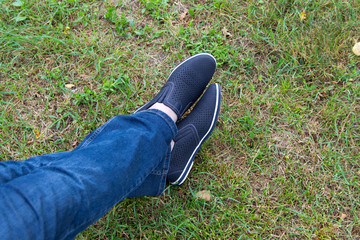 A man in jeans and summer shoes on the background of green grass . Loafers.