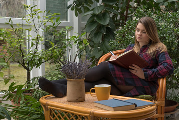 Beautiful young woman is writing her diary in winter garden