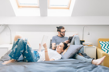 Wall Mural - Young couple reading a book in bed 