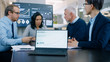 © Gorodenkoff - In the Meeting Room Laptop Standing on the Conference Desk Shows Company's Annual Growth Report with Interactive Charts. In the Background Business People Have Important Discussion.