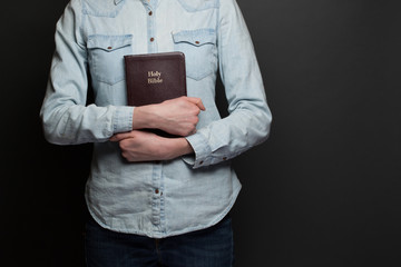 Wall Mural - Woman holding a Bible in hands wearing casual clothes over gray backgound