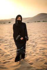 Wall Mural - Arabian Muslim woman in traditional dress walking through the desert.