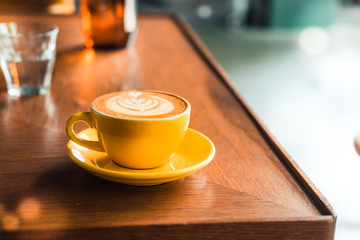 Flat white coffee in yellow cup  on a wooden table at the hipster coffee shop. Latte art concept. Vintage color filter effect. Copyspace