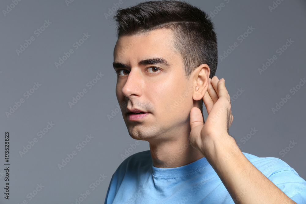 Young man with hearing problem on grey background