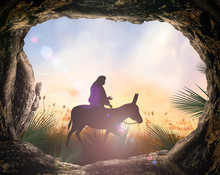 Palm Sunday Concept: Silhouette Jesus Christ Riding Donkey With Tomb Stone On Meadow Sunset Background