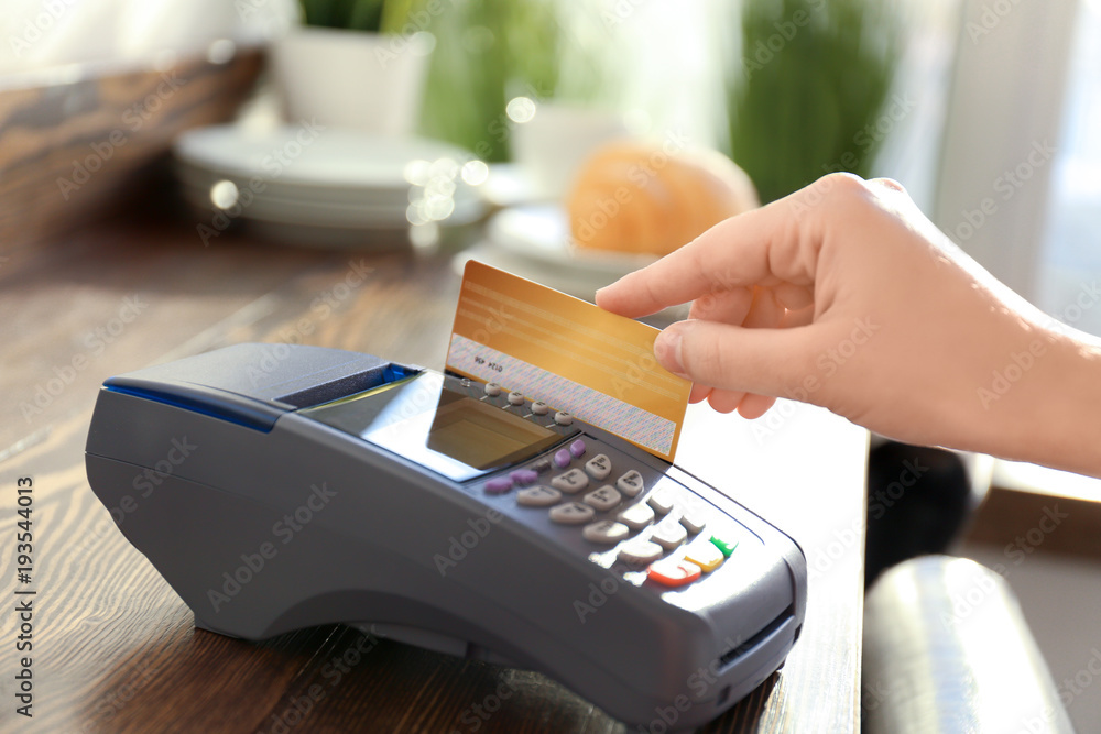 Woman using bank terminal for credit card payment in cafe