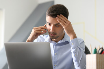 Sticker - Young man talking on phone while working with laptop in office