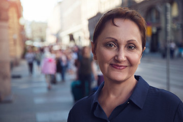 Professional headshot of a middle aged woman walking in city. Outdoor portrait of a middle aged female. Urban background. Street style shot. Filtered.