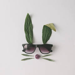 Wall Mural - Bunny rabbit face made of natural green leaves with sunglasses on bright background. Easter minimal concept. Flat lay.