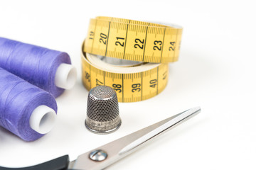 Wall Mural - Sewing accessories and tools, medium purple sewing threads, yellow measuring tape with black numbers, scissors and metal thimble on a white background