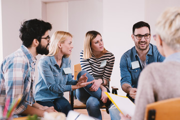 Young persistent handsome guy sharing a good news with other participants on special group therapy.