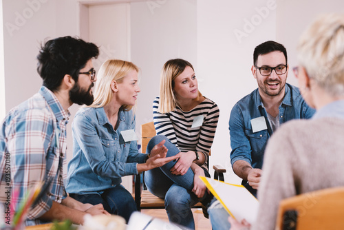 Fotomural Young persistent handsome guy sharing a good news with other participants on special group therapy