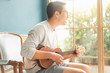 Asian young man hands playing acoustic guitar ukulele at home. Enjoy playing acoustic guitar sunshine in the evening..