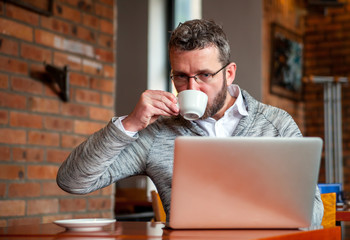 Wall Mural - Middle age man using laptop in cafe and drinking coffee