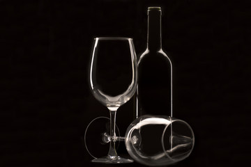 two wine glasses, one of them lying down and bottle of wine with black background