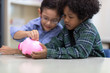© Nattanon - Selective focus at pig jar. Kids playing collect money with a pink saving Pig Jar in the Library. Setup studio shooting.