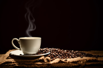 Wall Mural - Cup of coffee with smoke and coffee beans on black background