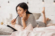 © deniskomarov - Young asian girl lying in bed, relaxing in her bedroom and write notes. Asian female student doing homework in bed. Girl in casual dress writing diary or studying in bed thinking.