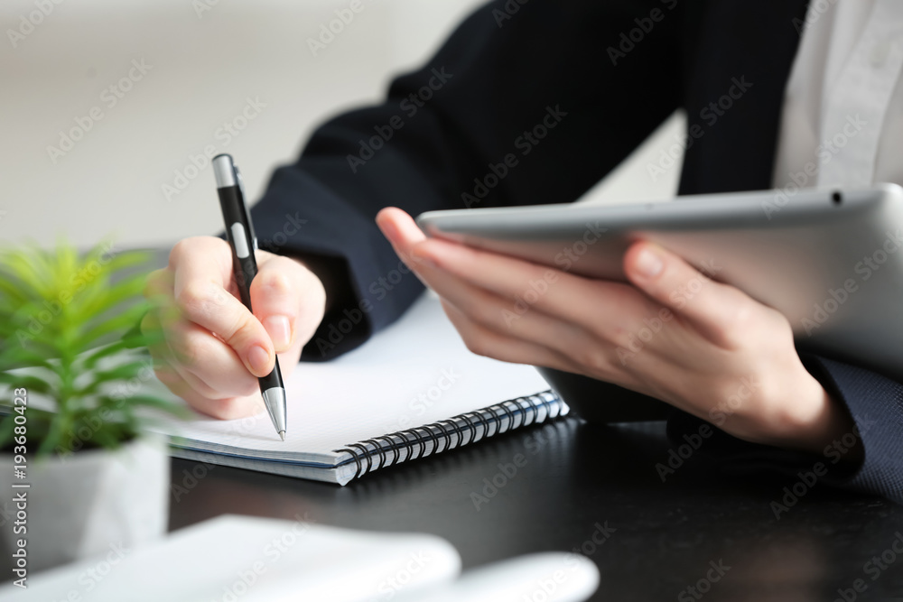 Female student with tablet computer writing in notebook at table, closeup. Studying process