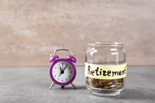 Coins In Glass Jar With Label "RETIREMENT" And Alarm Clock On Table. Pension Planning